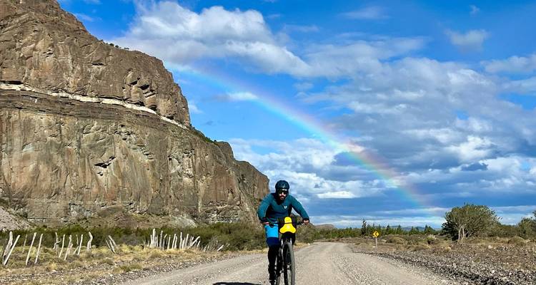 Cycliste sur un chemin de terre avec un arc-en-ciel dans le ciel.