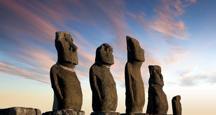 Quatre statues moaï de l'île de Pâques au coucher du soleil avec un ciel coloré.
