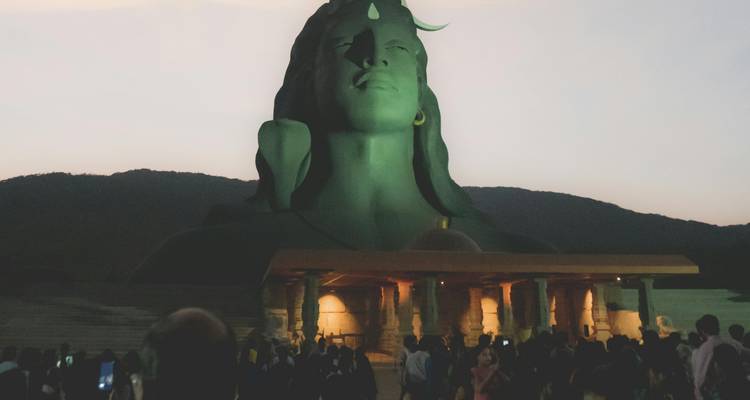 Estatua en un parque al atardecer con gente reunida.