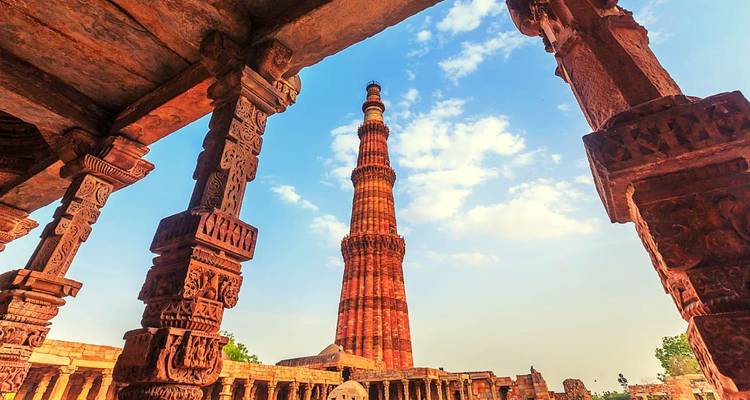 Blick auf den Qutub Minar, umgeben von kunstvoll geschnitzten Steinsäulen.