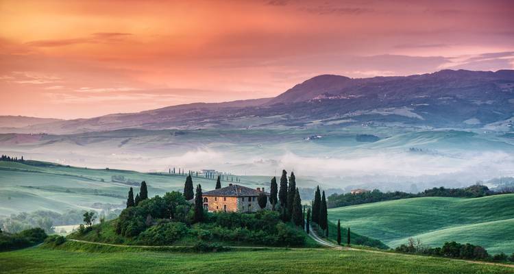 Colinas brumosas de la Toscana con una casa rodeada de cipreses.