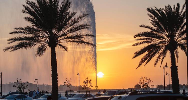 Fuente en Jeddah con palmeras y un atardecer de fondo.