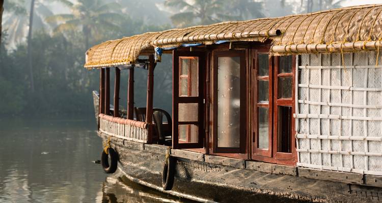 Une péniche traditionnelle du Kerala amarrée sur des eaux sereines au milieu d'une végétation luxuriante.