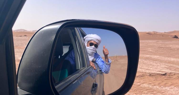 Persona dando pulgar hacia arriba desde la ventana de un coche en el desierto.