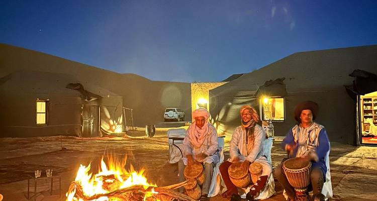 Hombres con vestimenta del desierto tocando tambores junto a una fogata.