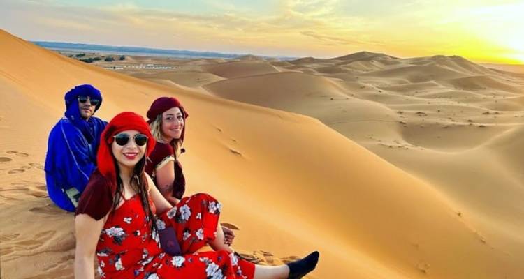 Personas sentadas en dunas del desierto al atardecer.