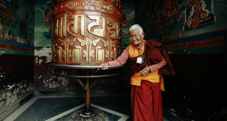 Bejaarde monnik die een groot gebedswiel draait in een tempel.