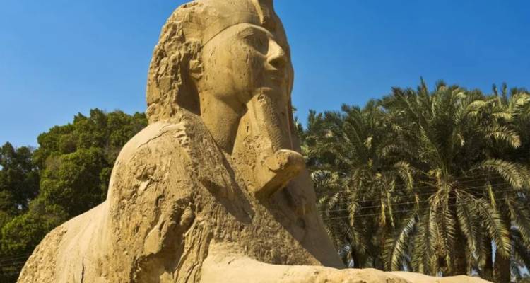 Gros plan d'une statue de sphinx avec des palmiers en arrière-plan.