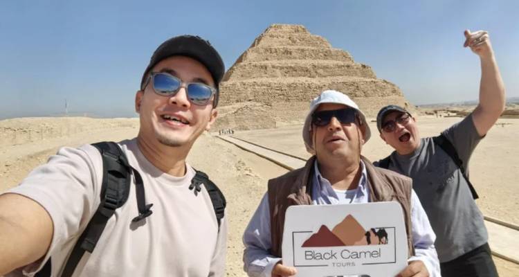 Groupe de touristes devant une pyramide tenant un panneau de visite.