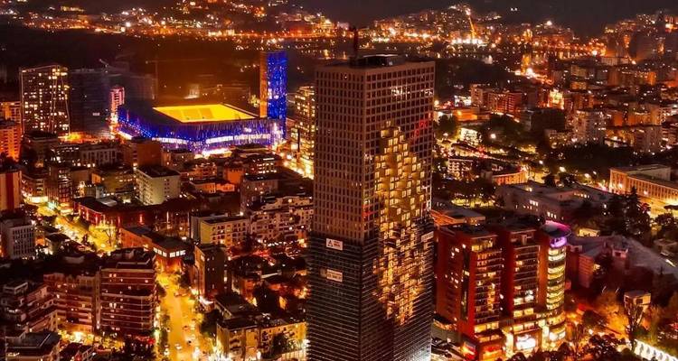 Vista nocturna de una ciudad con edificios iluminados y estadio.