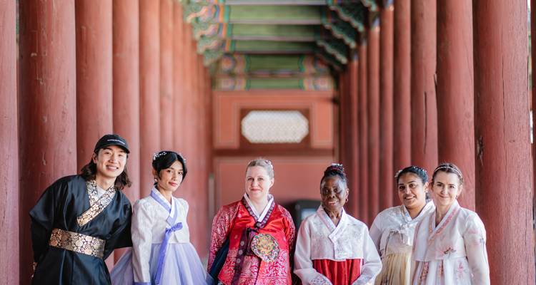 Grupo vistiendo hanbok tradicional posa entre columnas de madera roja de un corredor de palacio histórico coreano
