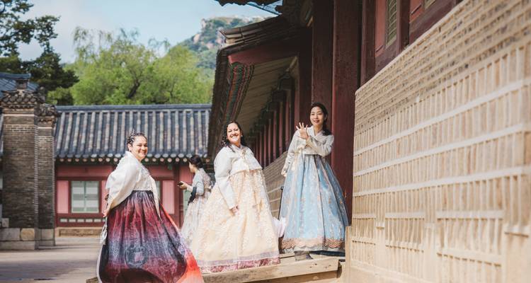 Tres mujeres con hanbok coloridos disfrutan del patio de un palacio tradicional coreano en un día brillante