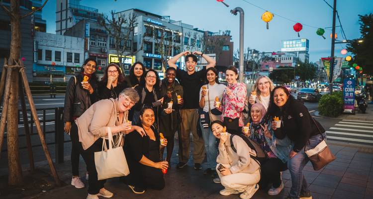 Grupo grande de turistas posando en una calle de la ciudad por la noche sosteniendo bocadillos bajo coloridos faroles colgantes