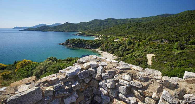 Vue côtière depuis une fortification en pierre avec une végétation luxuriante.