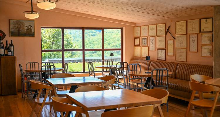 Un interior acogedor de un café o restaurante con mesas y sillas de madera, y certificados enmarcados en la pared.
