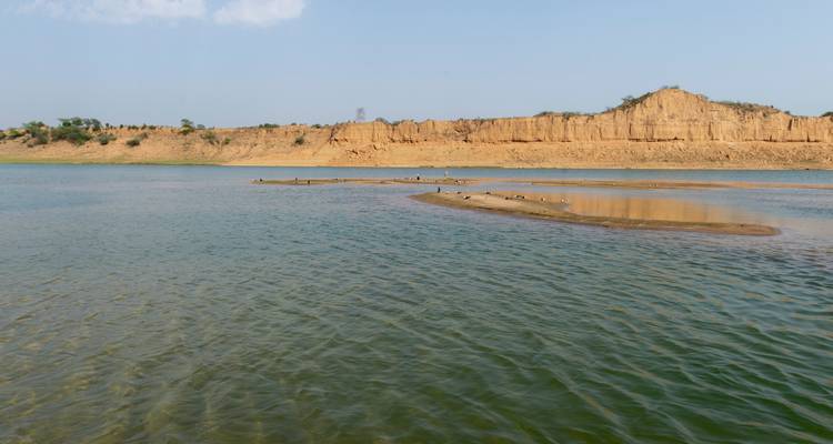 Large rivière bordée de falaises sableuses sous un ciel bleu clair