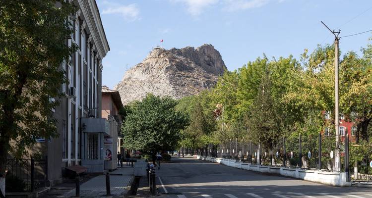 Straßenansicht mit Bäumen und Hügel mit einer Flagge im Hintergrund.
