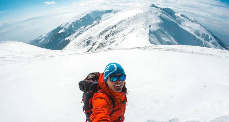 Escalador solitario sonriendo, rodeado de picos montañosos nevados.