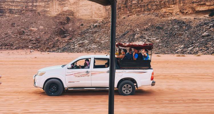 White 4x4 truck carries tourists across the red sand plains of Wadi Rum.