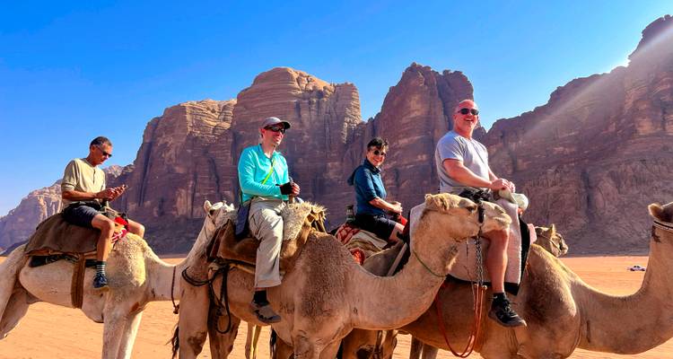 Four travellers ride camels against towering sandstone cliffs in Wadi Rum.