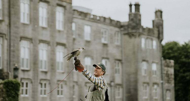 Halconero sosteniendo un ave rapaz fuera de un edificio histórico.