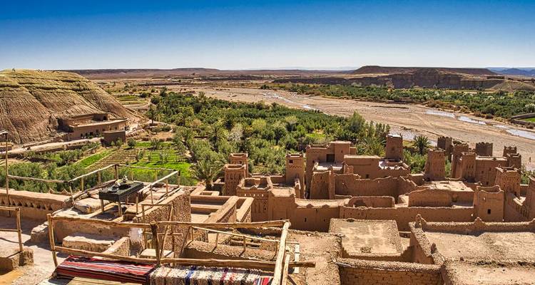Weite Ansicht eines traditionellen marokkanischen Dorfes mit einem Fluss und Wüstenlandschaft.