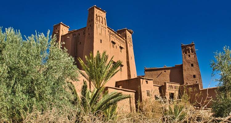 Eine traditionelle Kasbah in Marokko, umgeben von Palmen und Wüste.
