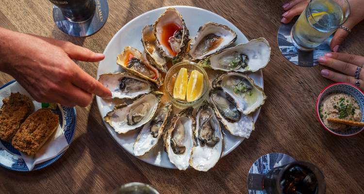 Plato de ostras con rodajas de limón y salsas para mojar.