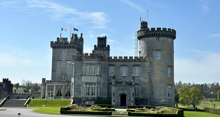 Majestuoso castillo de piedra con banderas ondeando y césped bien cuidado.