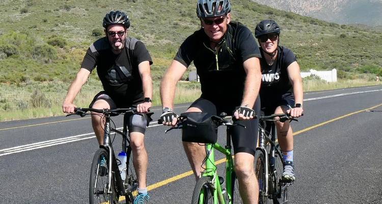 Trio de cyclistes souriants posant avec leurs vélos sur une route rurale.