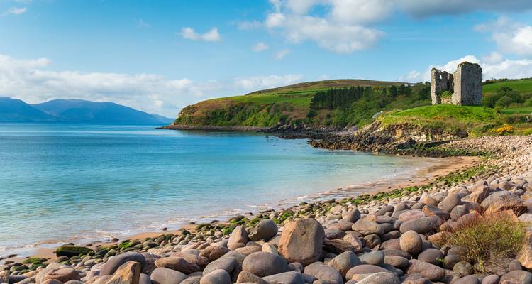 Ein steiniger Strand mit einer alten Ruine, die eine ruhige Bucht überblickt.