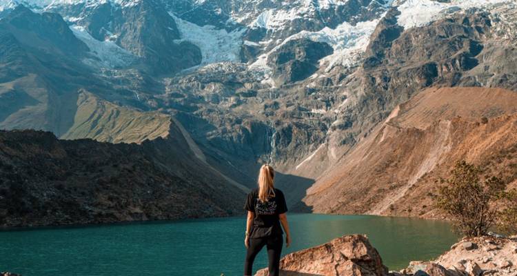 Persona de pie junto a un lago turquesa con montañas cubiertas de nieve