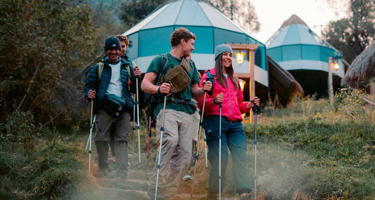 Grupo de excursionistas con bastones de trekking caminando junto a tiendas de campaña