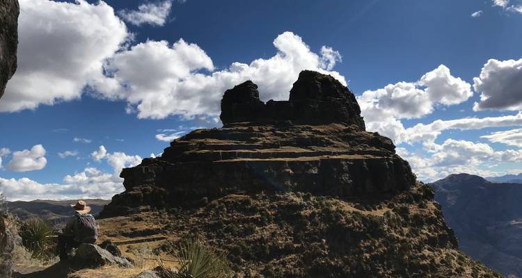 Persona sentada cerca de una formación rocosa bajo un cielo azul claro.
