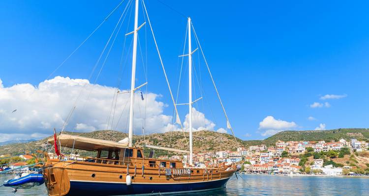 Barco de vela en un puerto con un pueblo costero al fondo.
