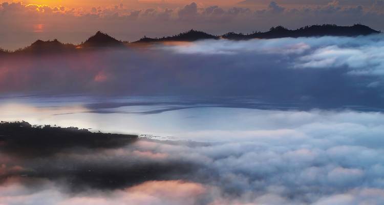 Mar de nubes al amanecer envolviendo las crestas volcánicas del Monte Batur con un cálido resplandor naranja.