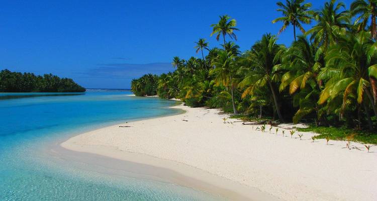 Idyllisch witZandstrand dat zich uitstrekt rond een turquoise lagune met palmbegroeid eilandjes onder een levendige blauwe hemel
