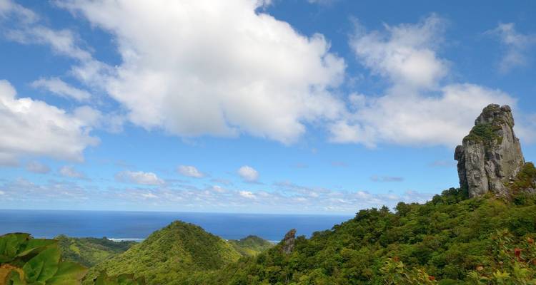 Groen bergachtig landschap met een ruige rotspartij die uitstijgt boven de jungle en oceaanhorizon