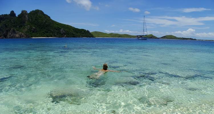 Personne nageant dans une eau cristalline avec des îles en arrière-plan.