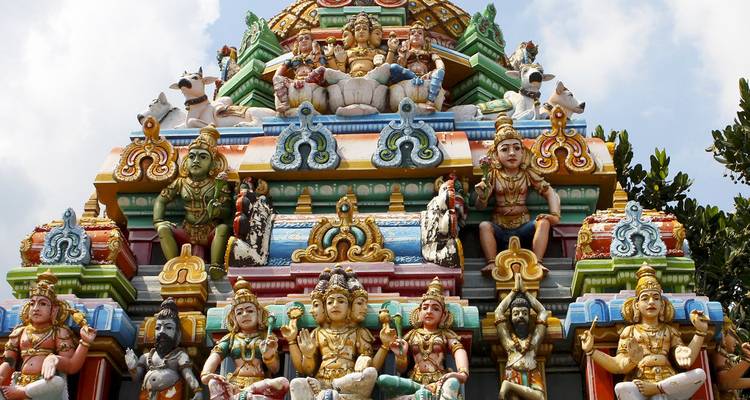 Gopuram de templo hindú pintado con colores vibrantes y adornado con deidades coloridas contra un cielo parcialmente nublado en Chennai.