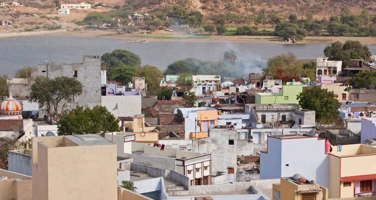 Asentamiento rural junto al río con casas de colores pastel y colinas secas más allá del Lago Pushkar.
