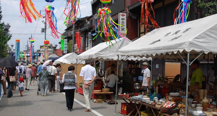 Lively Japanese street market with stalls selling antiques and colorful tanabata streamers decorating overhead wires.