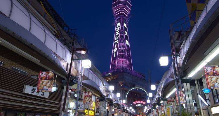 Night street view of Osaka’s Tsutenkaku Tower glowing purple above a lively shopping arcade.