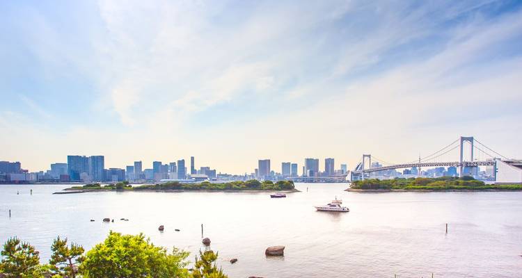 Tokyo Bay skyline with Rainbow Bridge and pleasure boats under a bright hazy sky.