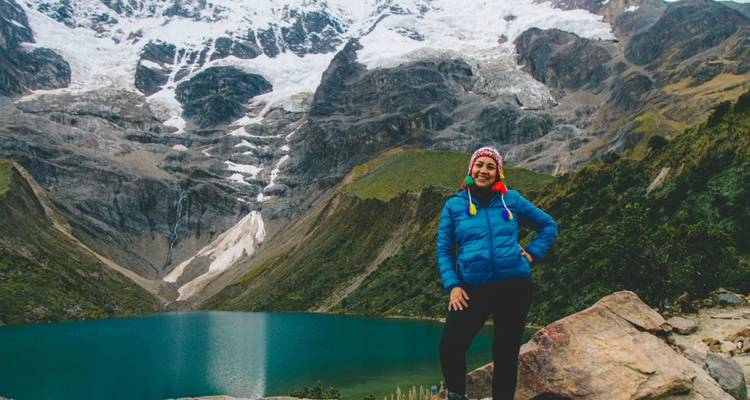 Personne posant près d'un lac glaciaire avec des montagnes enneigées.