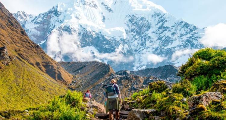 Randonneurs marchant sur un sentier de montagne aux sommets enneigés.