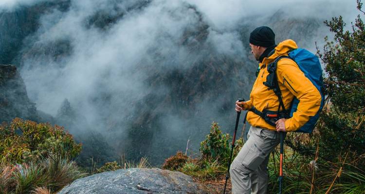 Randonneur en veste jaune contemplant un paysage montagneux brumeux.