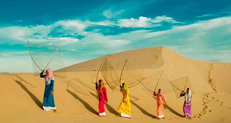 Des femmes en tenue colorée marchant dans un désert en portant des filets.