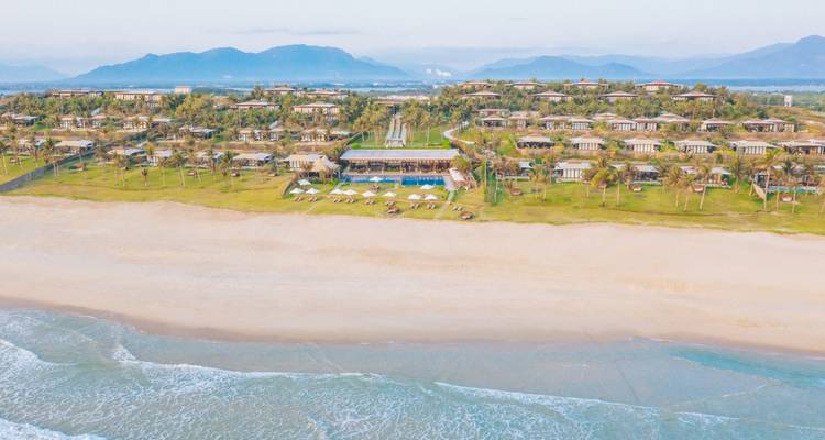 Vue aérienne d'un complexe hôtelier en bord de mer avec des villas dispersées.