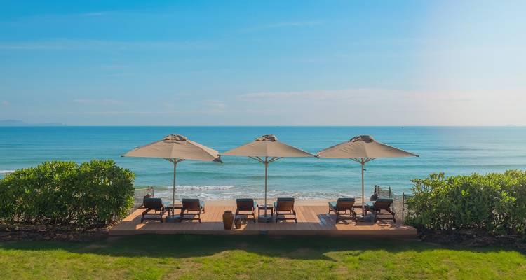 Terrasse de plage simple avec transats face à la mer sous des parasols.